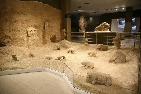 A display at the Gobeklitepe site museum sets small carved Neolithic animal figures across a sandy floor beside a railed walkway.