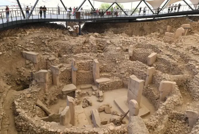 Visitors line the raised walkway above the Gobeklitepe excavation where several enclosures of T-shaped pillars lie exposed.