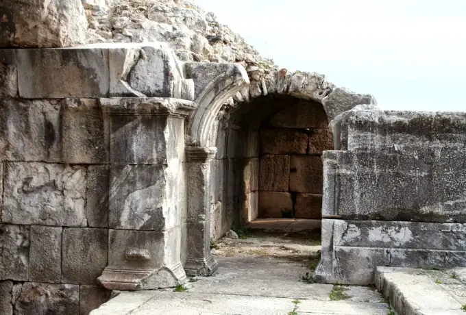 A carved arched doorway leads through massive stone walls in the ruins of ancient Miletus.