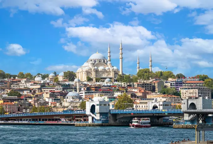 From the water, the Galata Bridge crosses the Golden Horn in Istanbul below a hillside crowned by a domed mosque.