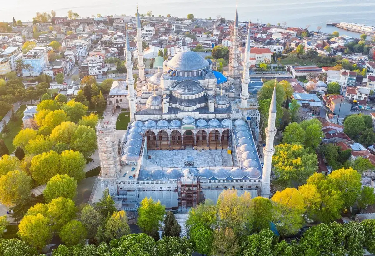 An aerial view of the Blue Mosque in Istanbul shows its domes, six minarets and full arcaded courtyard ringed by autumn trees.