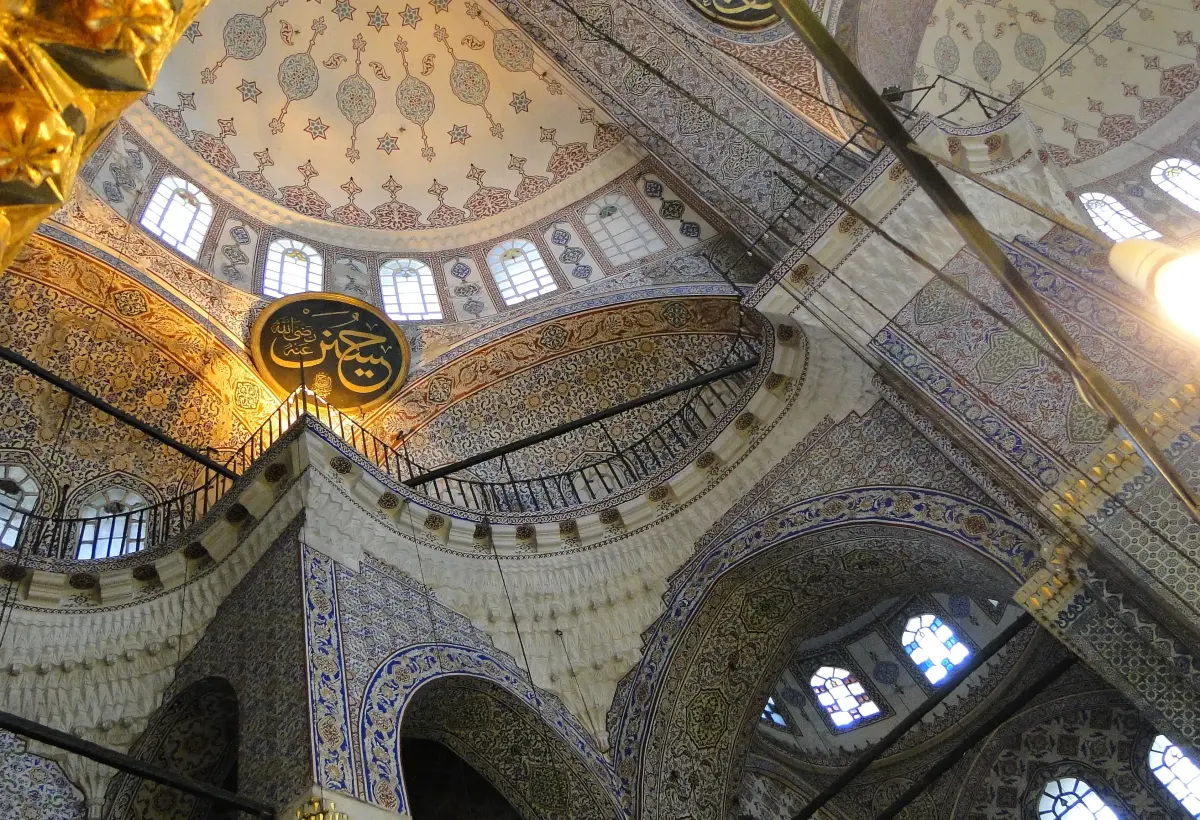 Painted vaults, arches and tiled panels curve overhead inside the Blue Mosque in Istanbul with stained glass in the windows.