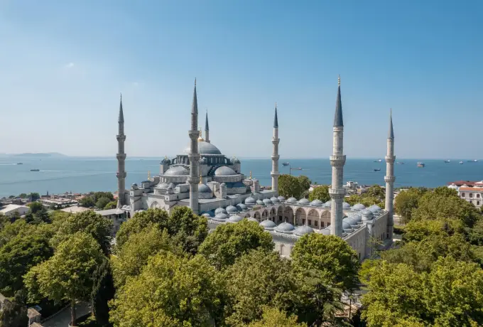 The Blue Mosque in Istanbul sits above a green park with the pale Sea of Marmara stretching out beyond it.