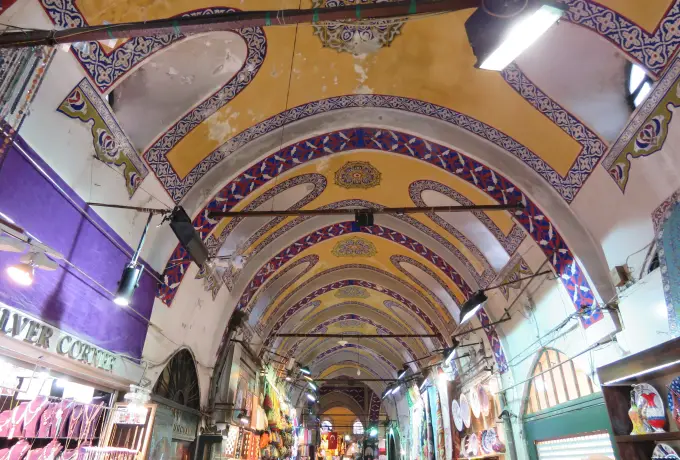 A yellow and blue painted vault arches over a busy passage of clothing and sweet shops in the Grand Bazaar in Istanbul.
