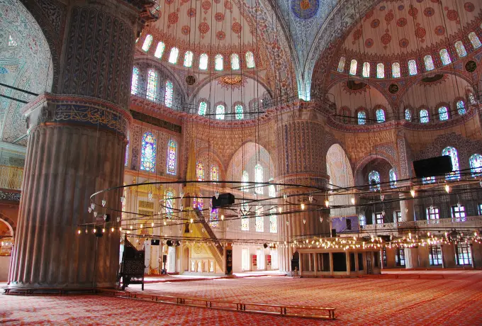 A tall fluted pier rises beside the carpeted floor of the Blue Mosque in Istanbul under its painted arches and windows.