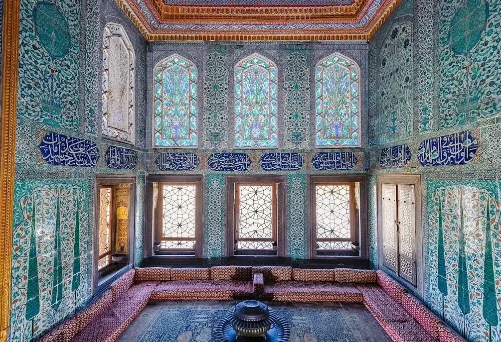 Turquoise and blue Iznik tiles cover the walls around tall stained glass windows in a room at Topkapi Palace in Istanbul.