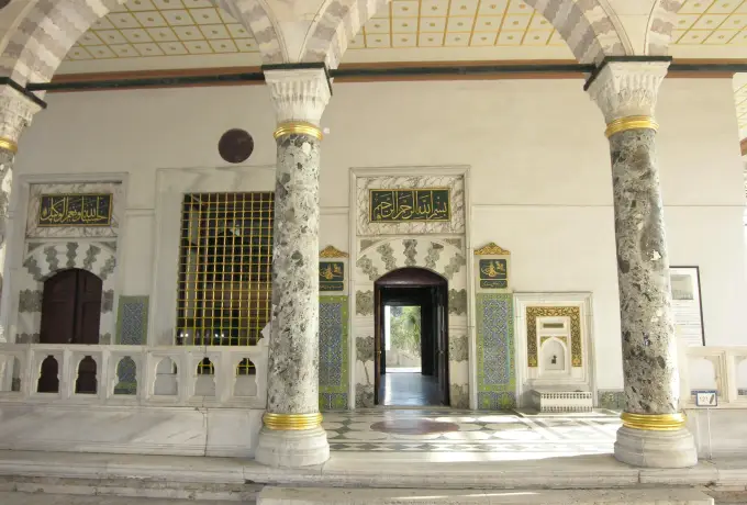 Veined marble columns carry the arches of a portico at Topkapi Palace in Istanbul in front of a carved doorway.