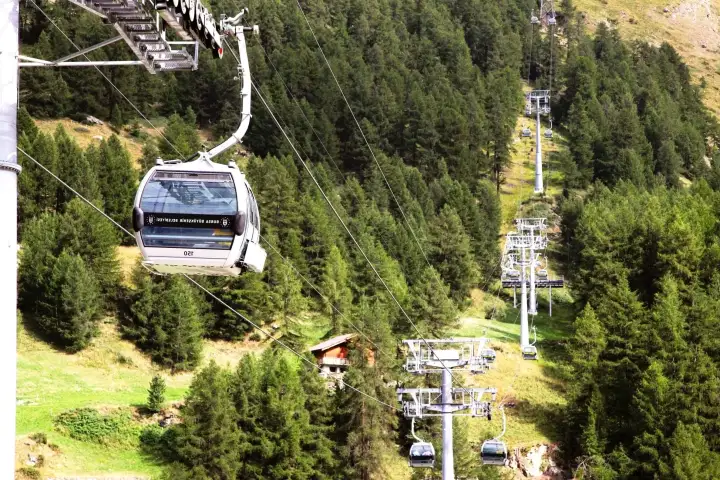 A cable car cabin climbs above dense pine forest on the Uludag line at Bursa, the steel pylons and a second lift running up the green mountainside below.