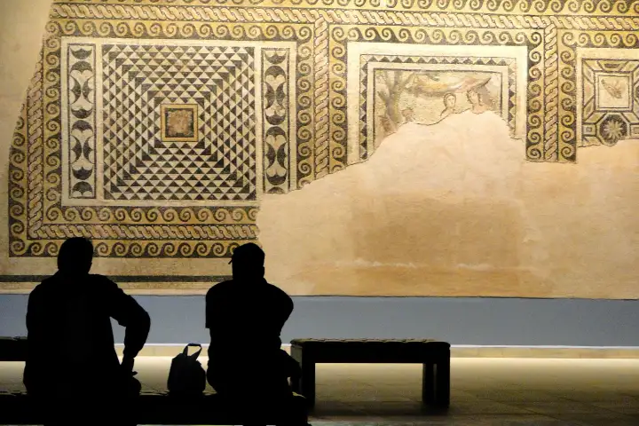 Two visitors sit in silhouette in front of a large mounted Roman mosaic panel in the Zeugma museum at Gaziantep.
