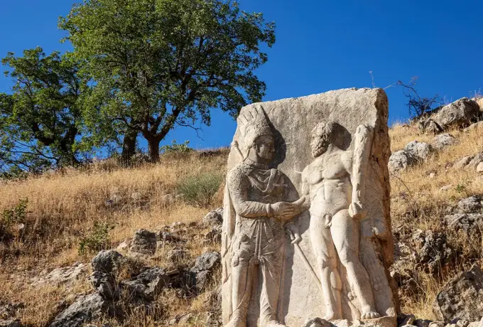 A weathered stone relief on a dry hillside at Arsameia in Adiyaman shows two standing figures clasping hands.