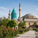 Turquoise dome of the Mevlana Museum beyond a rose garden in Konya