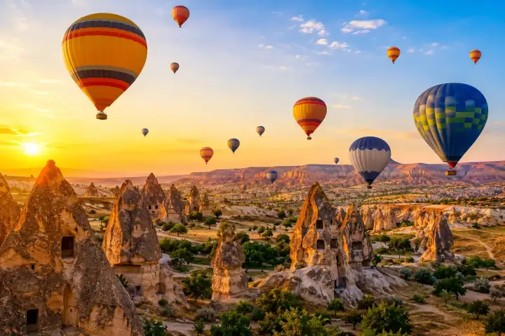 Colorful hot air balloons fly above Cappadocia's fairy chimneys in golden morning light.