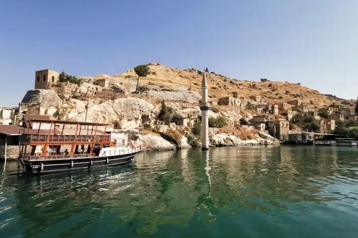 A tour boat beside Halfeti's submerged mosque minaret and stone village on the Euphrates.