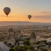 Five hot-air balloons above pale rock ridges in warm early sunlight